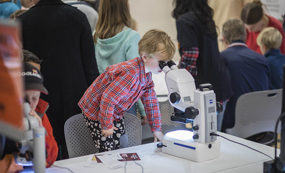 En liten pojke tittar i ett mikroskop under ForskarFredag i Umeå